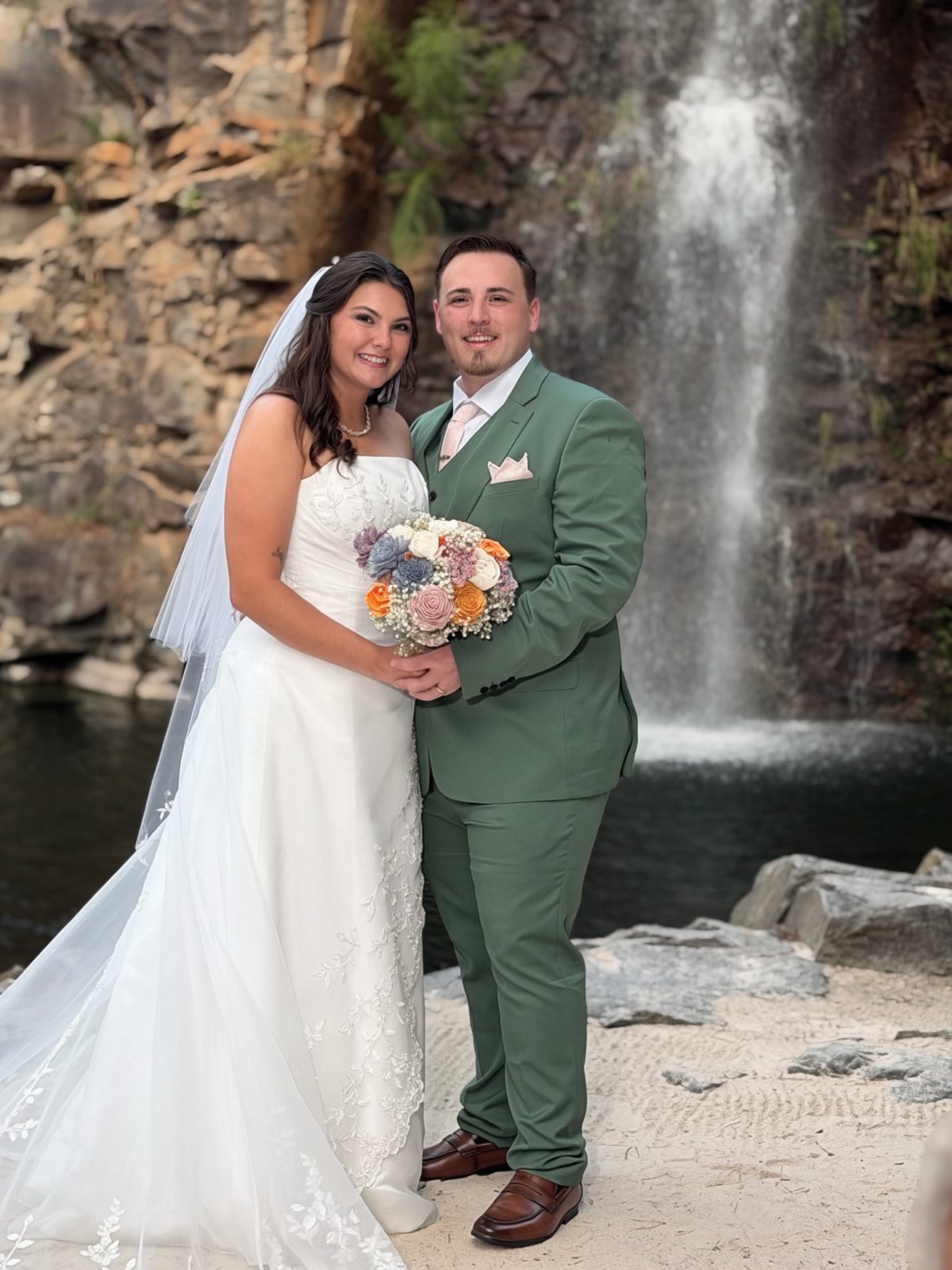 Ashleigh and Robert smiling together in front of the waterfall at Carrigan Farms